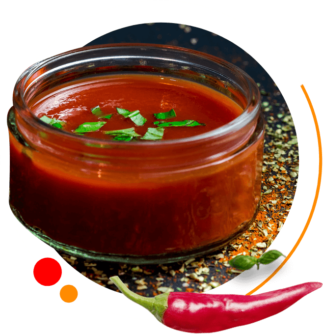 A bowl of chili sauce with a red pepper in the background.