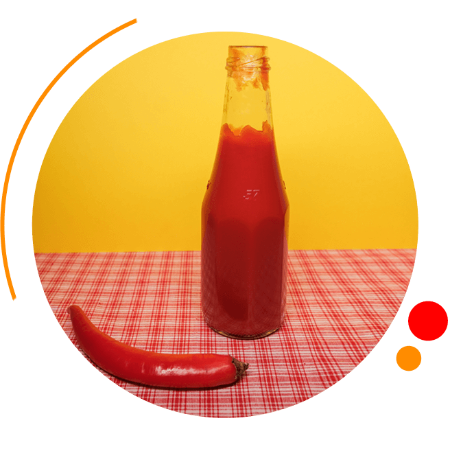 A bottle of ketchup and a chili pepper on a table.